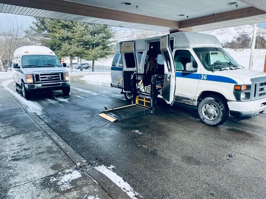 Two ATS vans at a facility entrance in the snow, one with its wheelchair ramp lowered